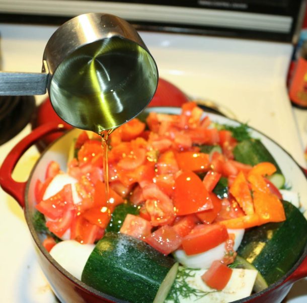 Pour olive oil into briam ingredients