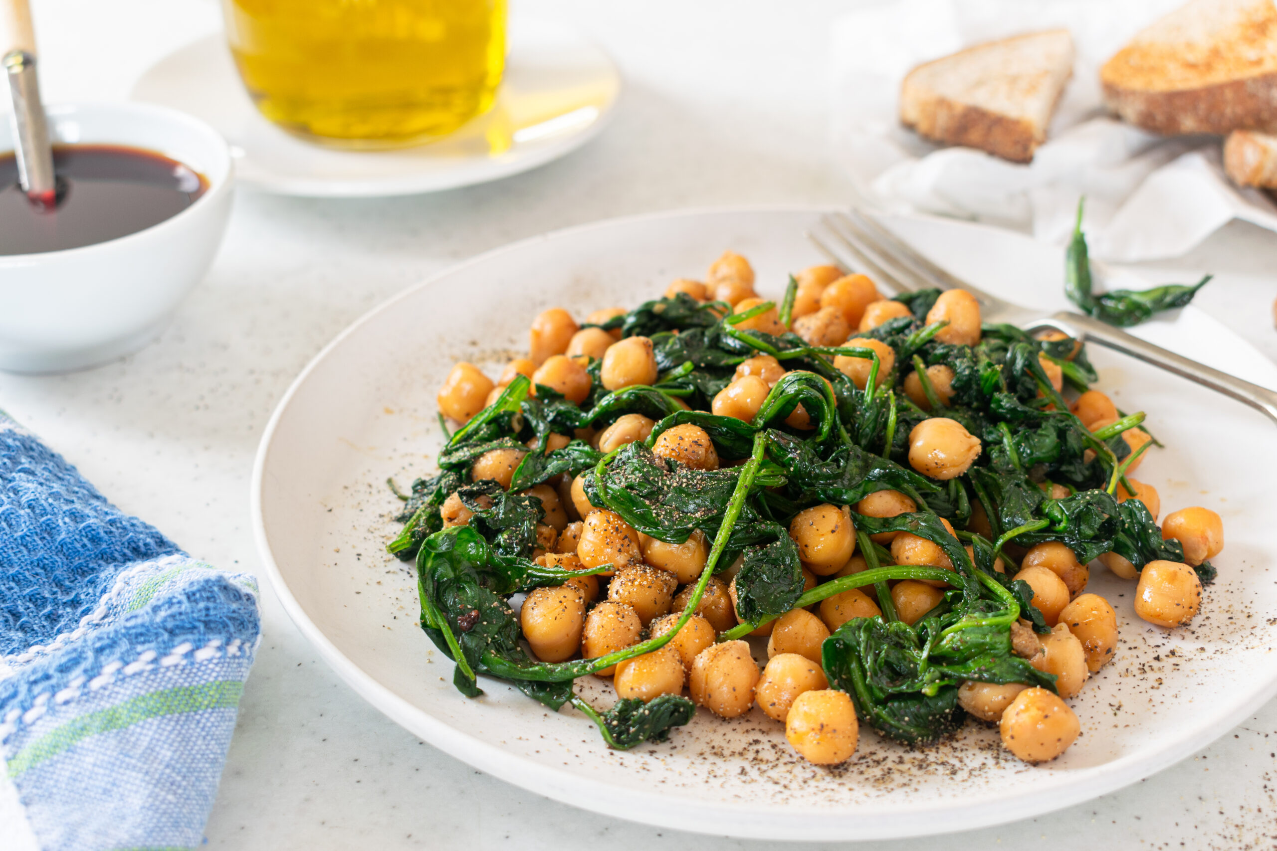 Espinacas con Garbanzos on a white plate, chickpeas and spinach cooked with garlic and paprika, with bread and olive oil in the background.