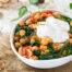 A bowl of Mediterranean chickpea stew with spinach, tomatoes, rice, and herbs, topped with a generous dollop of Greek yogurt.