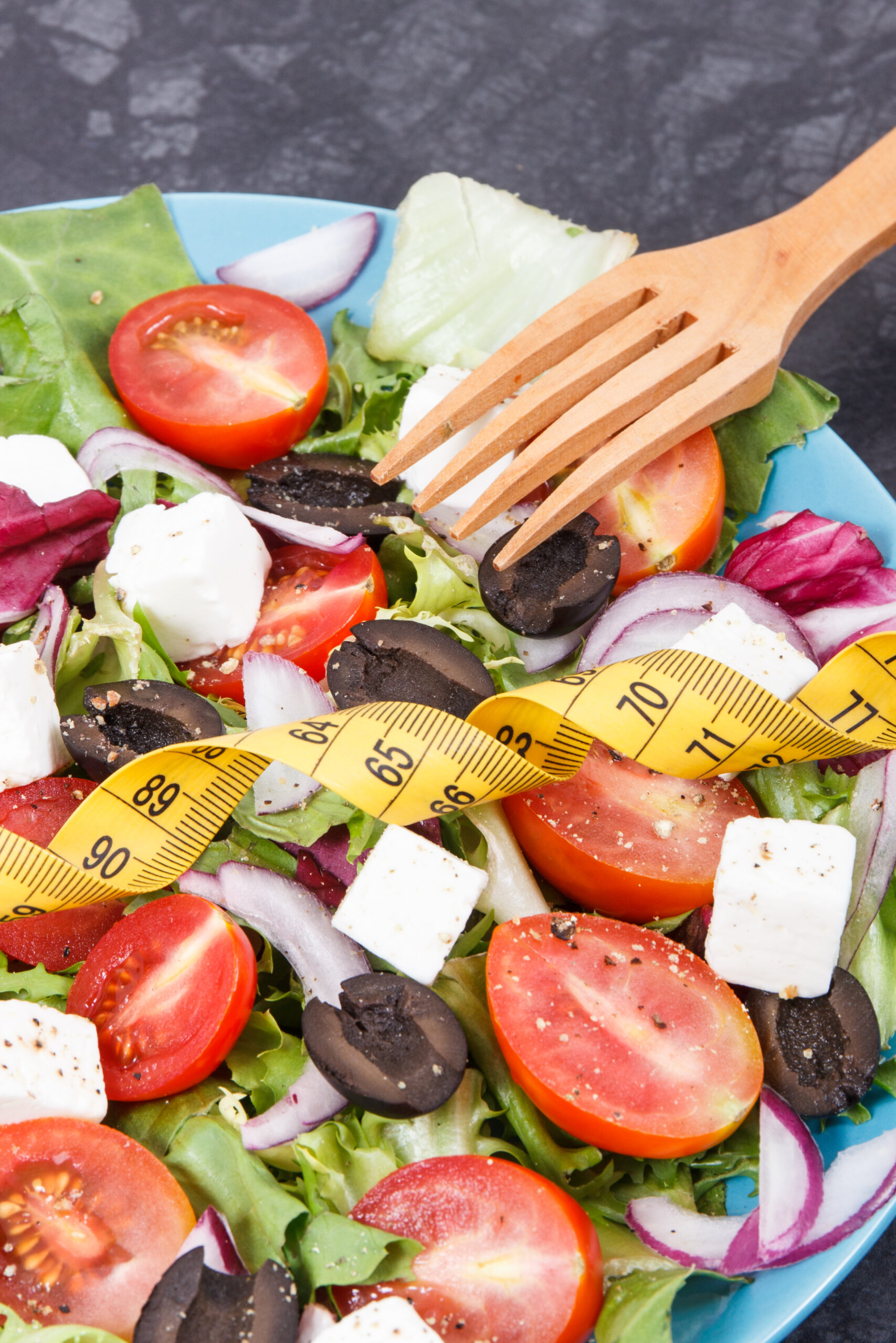 Tape measure and fresh greek salad with feta cheese and vegetables. Healthy meal as source natural vitamins